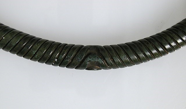 Detailaufnahme der glatten Oberfläche eines sogenannten unechten Wendelhalsringes. Die Einritzungen in den runden dunklen Kupferstab imitieren einen echten Wendelhalsring.