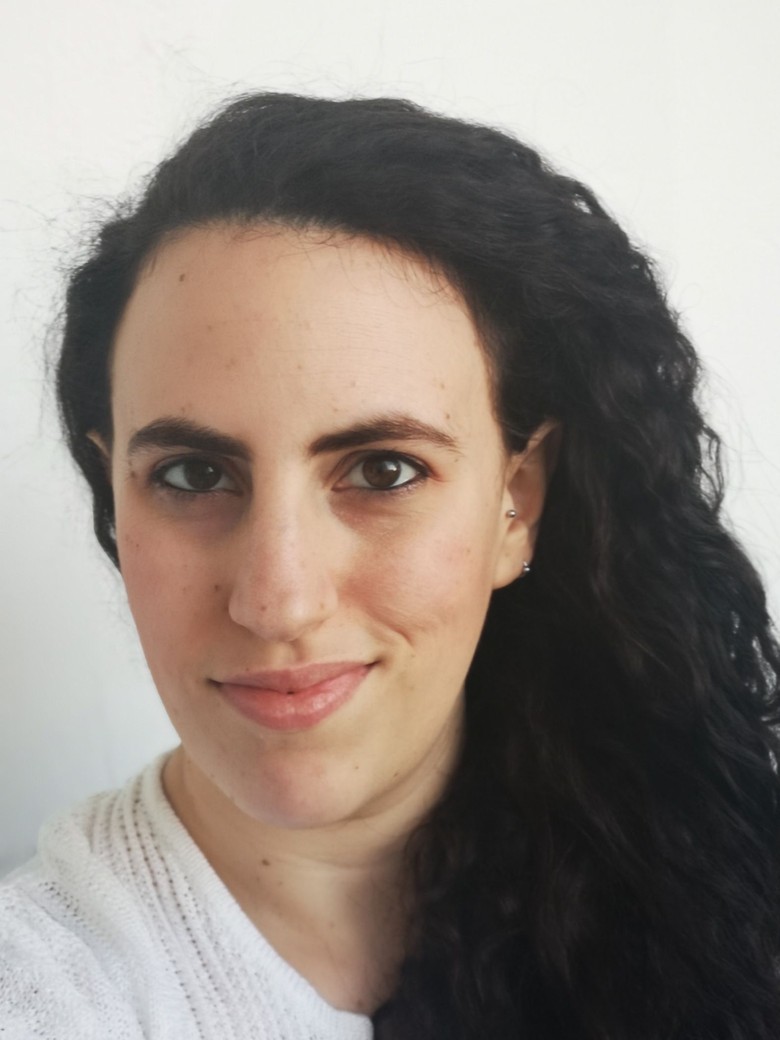 Eine Frau lächelt in die Kamera. Sie hat dunkle Augen und dunkle, lange Haare.