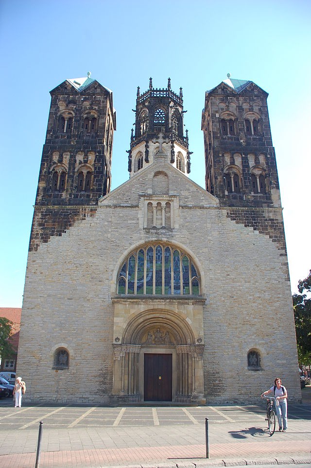 Auf dem Farbfoto, ist die Pfarrkirche St. Ludgeri mit Blick auf den Eingang zu sehen. Es wurde aus der Froschperspektive aufgenommen. Zudem sind die Türme dunkler als das Grundgebäude, was möglicherweise auf einen Umbau oder Erneuerung des Grundgebäudes schließen, folglich sind die Türme wahrscheinlich älter.