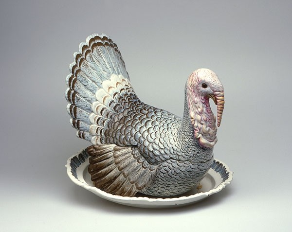 Das Bild zeigt eine Terrine in Form eines Truthahns. Die Terrine steht auf einem Teller und besitzt aufgemalte blaue und braune Federn.