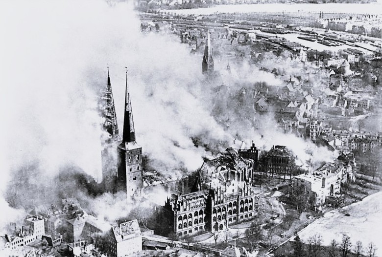 Zu sehen ist eine Zeichnung des Lübecker Doms, welcher stark verraucht ist. Die umliegenden Gebäude sind stark beschädigt und es steigt auch aus ihnen Rauch hinauf.