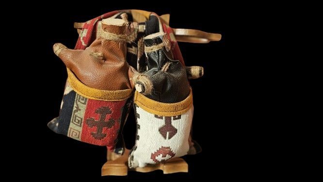 Ein Ständer mit zwei Ledersäcken, die mit Wein gefüllt sind. Die Säcke sind zum Teil mit Stoff überzogen, der bunt und verziert ist.