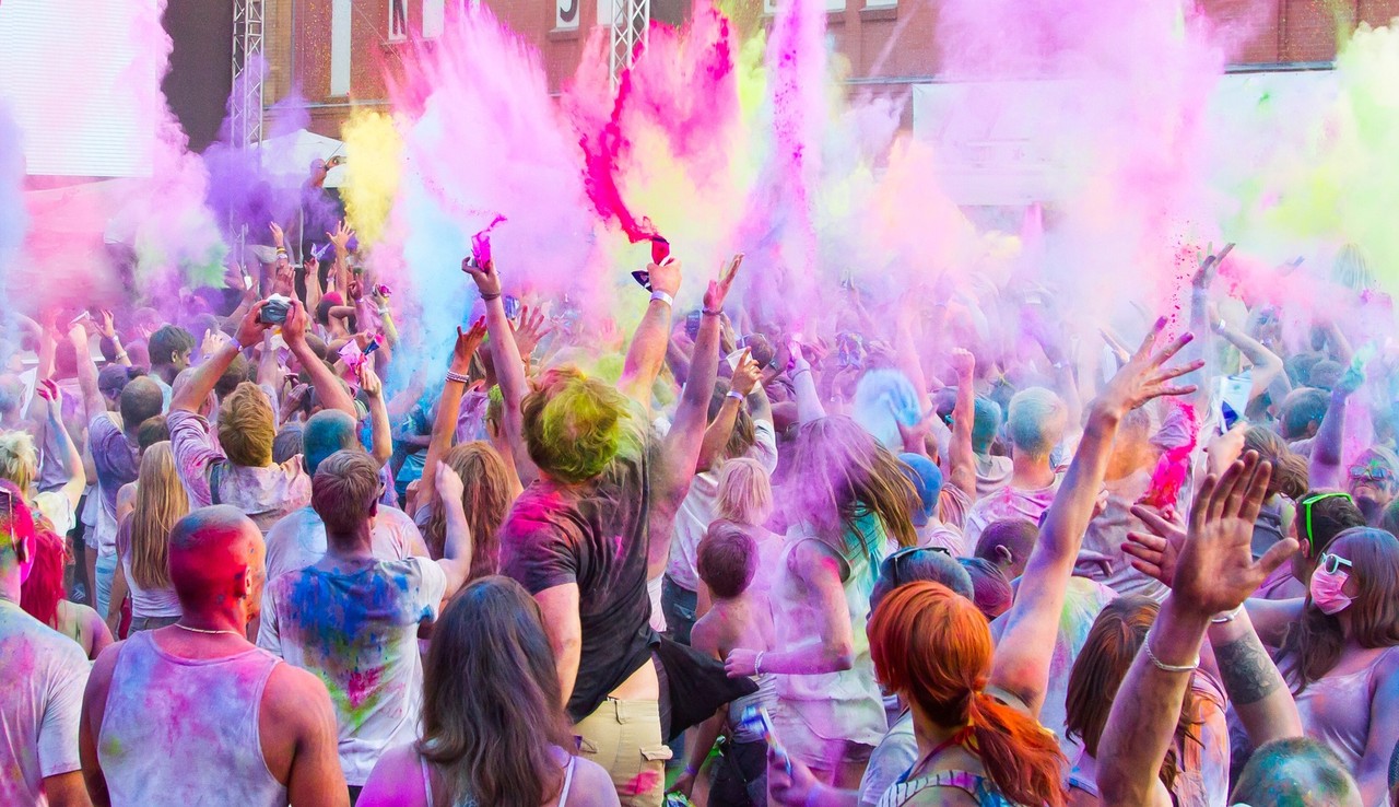 Auf dem Bild sind viele farbige Menschen die das Fest Holi feiern und bunten Pulver in die Luft schmeißen.
