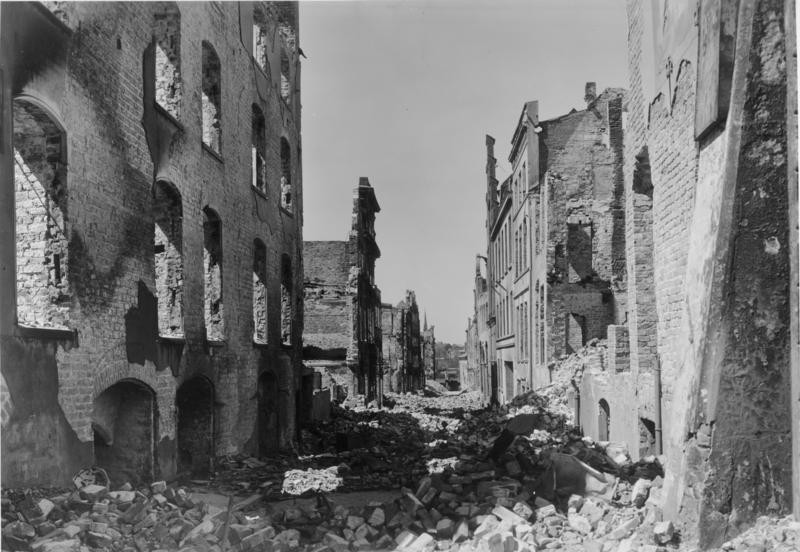 Zu erkennen ist die zerstörte Alfstraße. Auf der Straße liegen Trümmer von den zerstörten Häuserfronten. Einige Häuser sind eingestürzt.