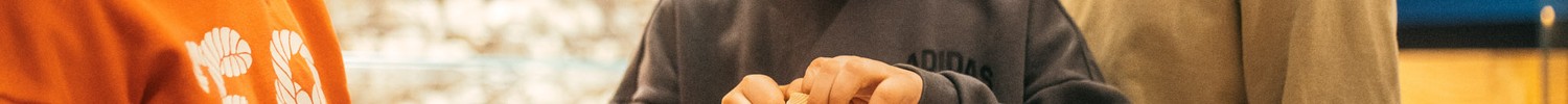 Kinder probieren einen Faden durch eine Muschel zu fädeln
