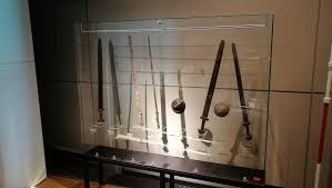 Das Bild zeigt eine Vitrine im LWL-Museum Herne, in der senkrecht stehend einige Spathae sowie mehrere Schildbuckel präsentiert werden.