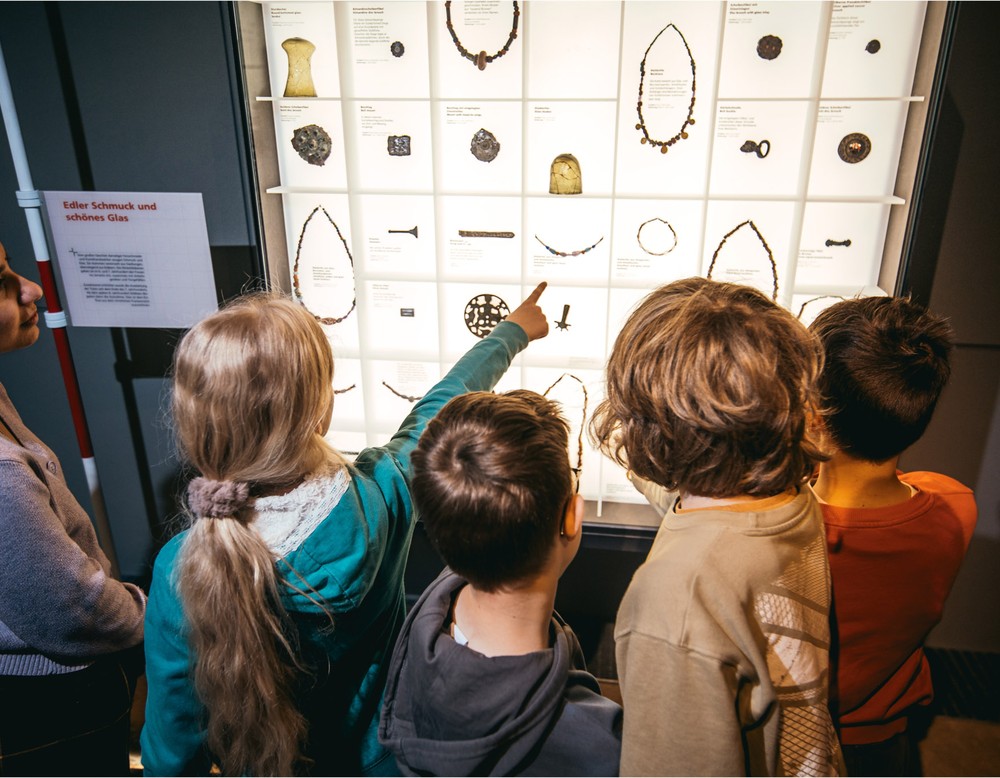 Eine Gruppe Kinder erkundet gemeinsam eine Vitrine mit Schmuck.