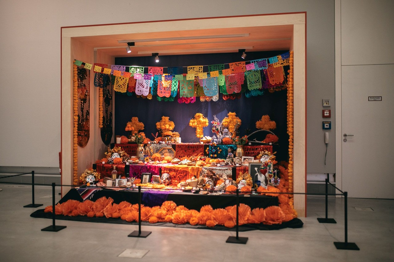 Auf dem Bild ist ein bunter Altar für die Toten zu sehen mit Girlanden, unechten Blumen und Gaben an die Toten.