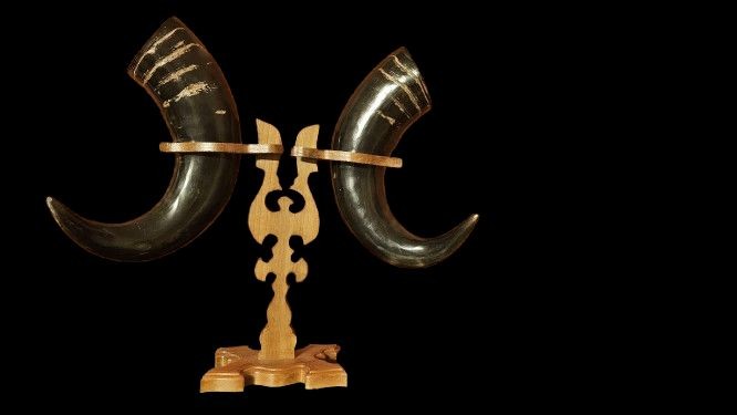 Zwei Trinkhörner, die auf einem Ständer stehen, vor schwarzem Hintergrund. Die Hörner sind gebogen und am oberen Rand mit Linien verziert.